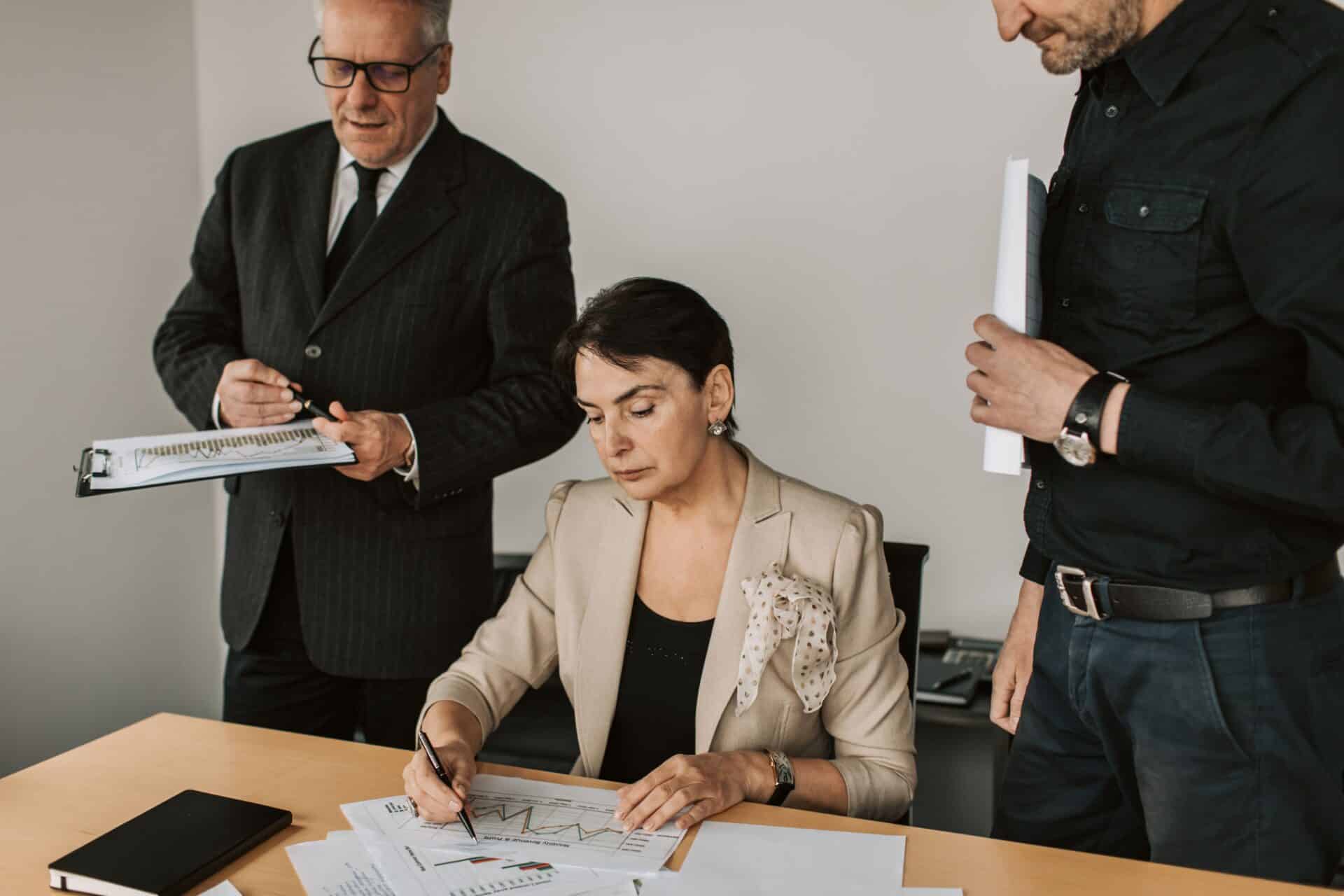 Three individuals in business attire collaborating over paperwork at a conference table.