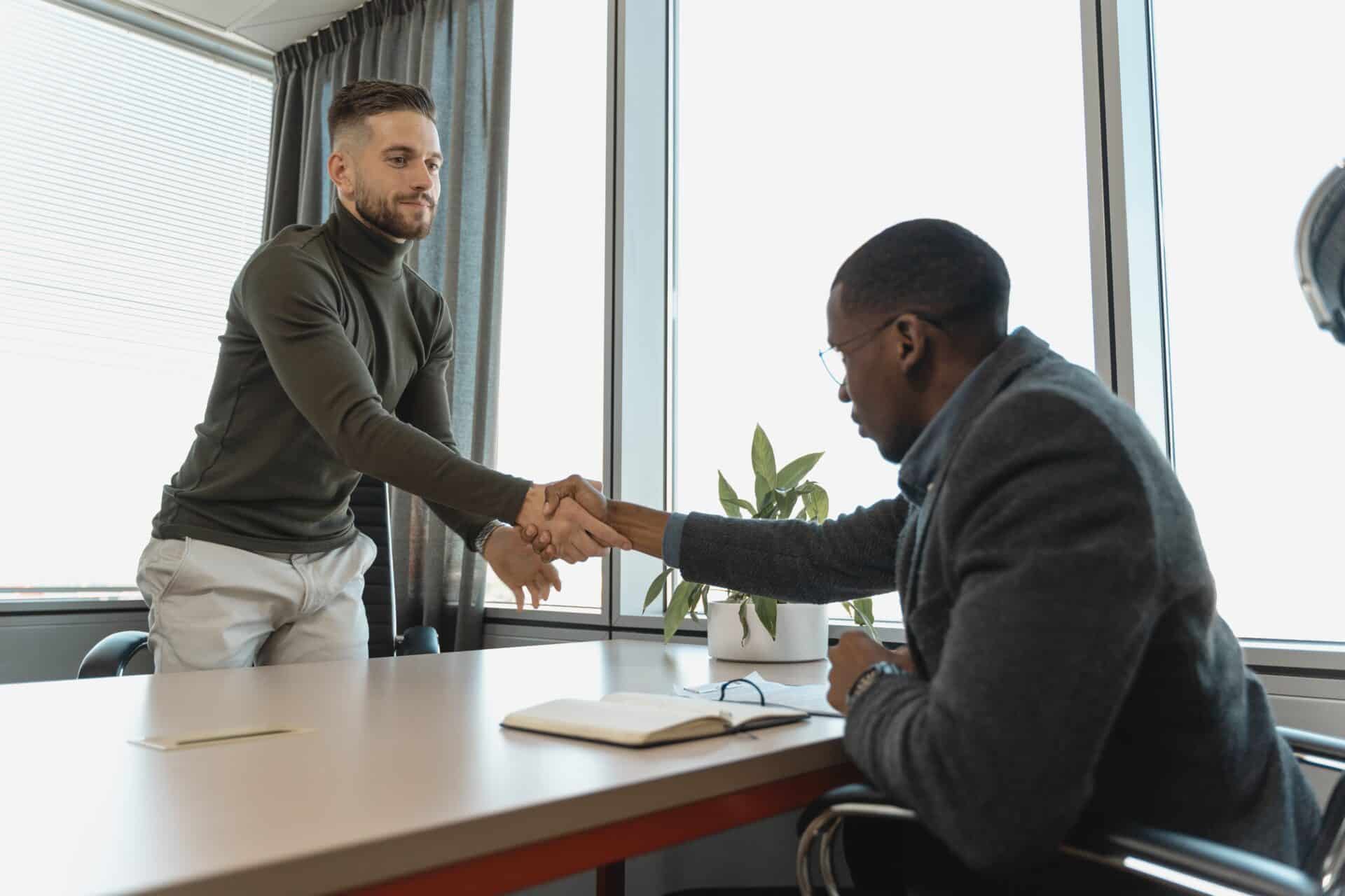 Two men shaking hands in an office setting, symbolizing a professional agreement or collaboration.