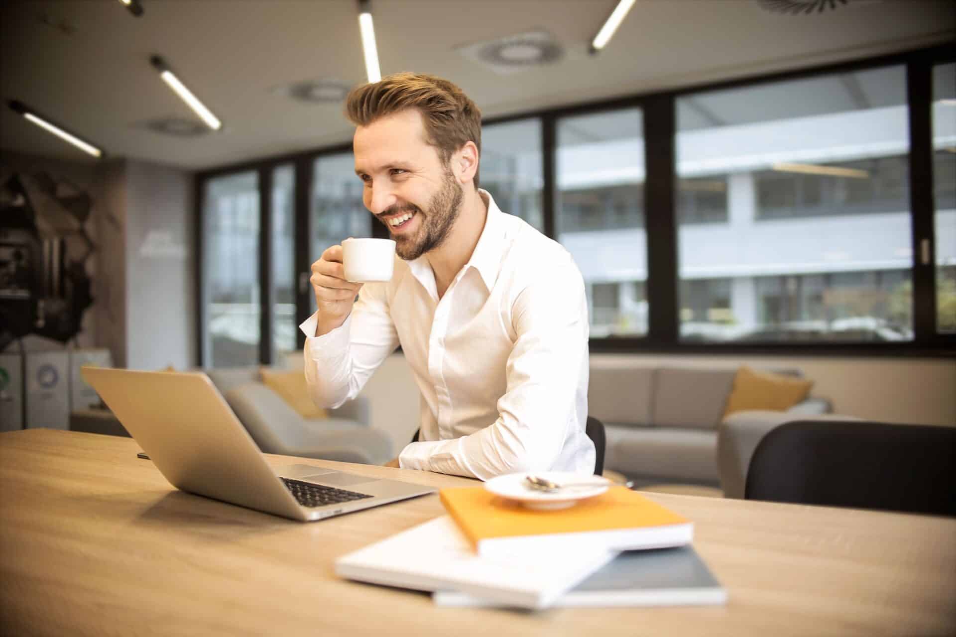 A man sits at a table with a laptop and coffee, focused on his work in a cozy café setting.