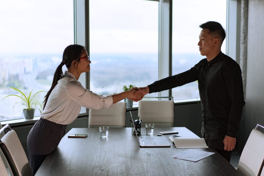 Two colleagues engaging in a handshake inside an office, representing a successful business interaction.