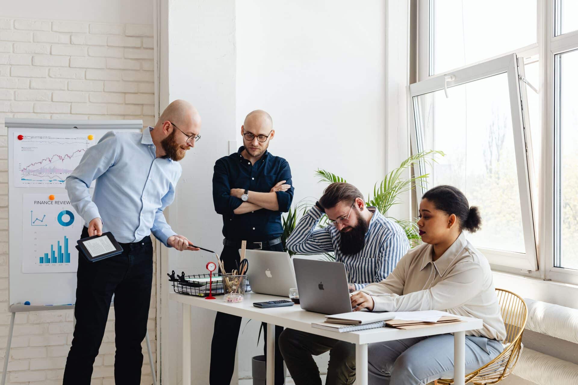 A group of five individuals gathered around a table, each using laptops, engaged in discussion and collaboration.